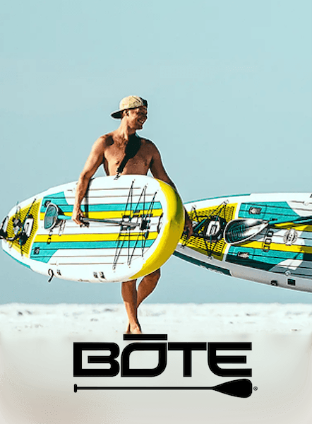 Bote paddleboard customer carrying two paddleboards on the beach with the BOTE wordmark below