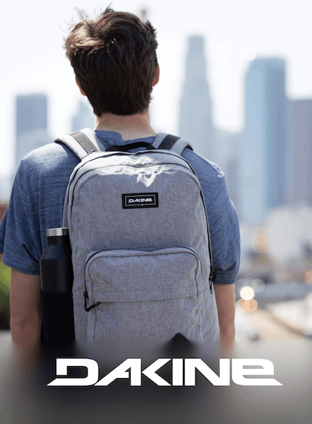 Person wearing a grey Dakine backpack with a city skyline in the background and the DAKINE wordmark below